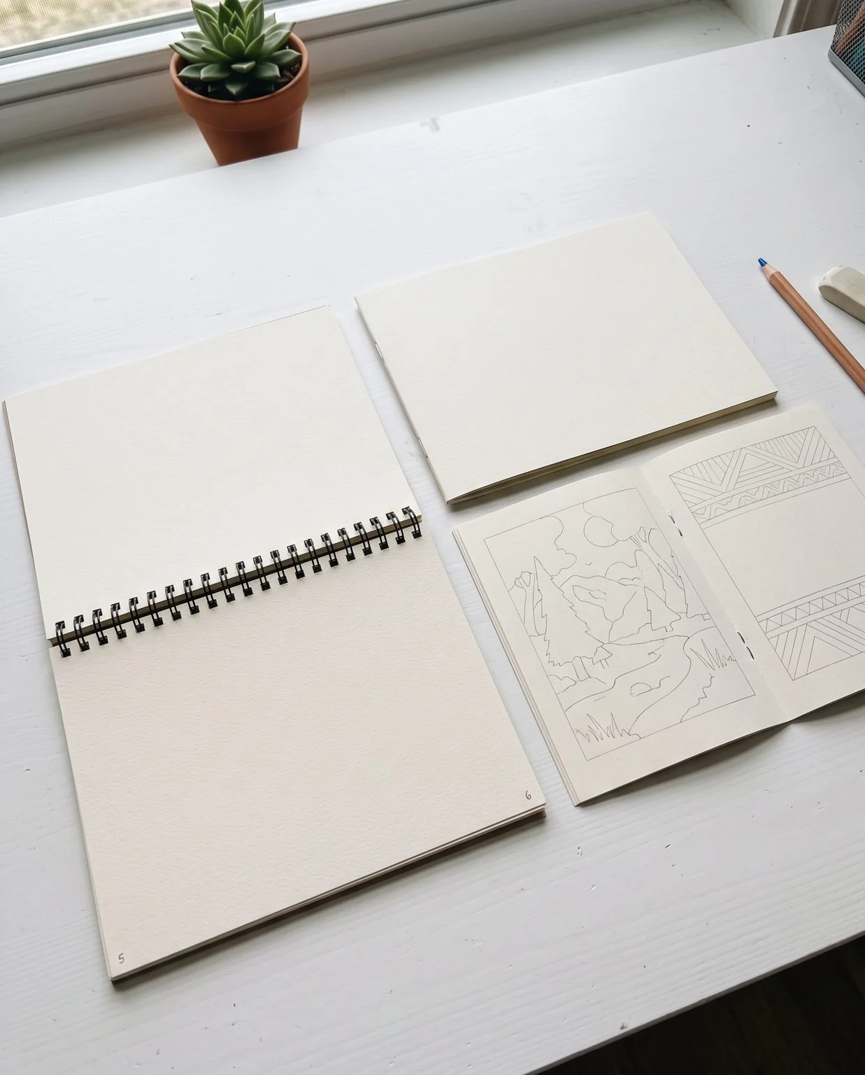 Two copies of the same coloring book side by side on a desk: one spiral bound lying open and flat, one stapled and closed